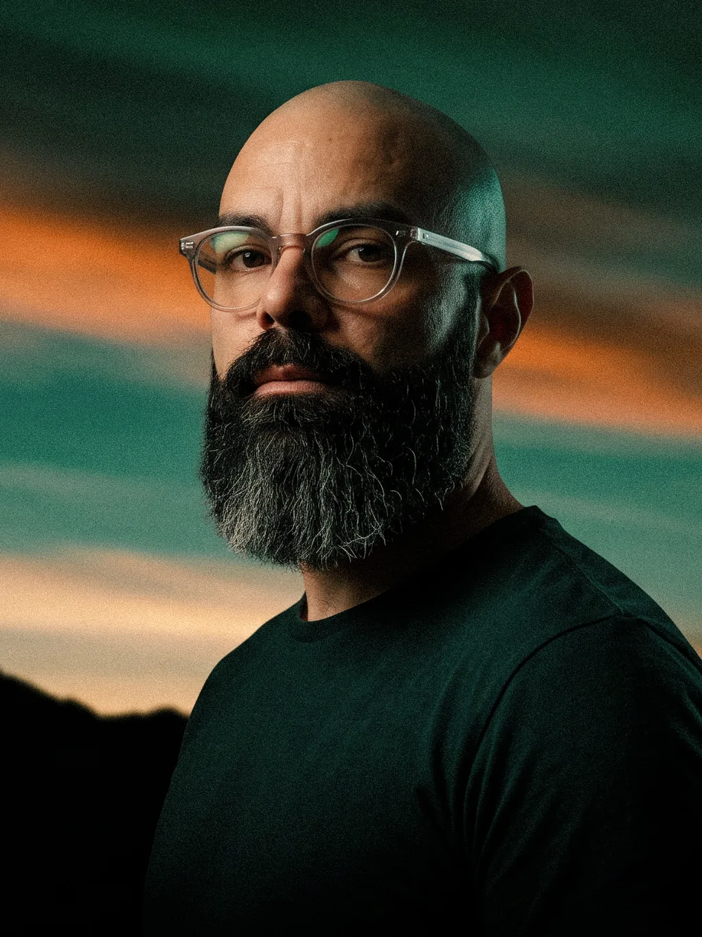 Retrato de Leo Becker, de óculos e barba, contra um céu ao entardecer